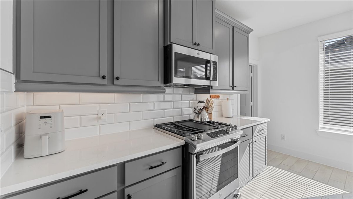 Modern kitchen with gas stove, microwave, and grey cabinets in a furnished home rental in Cypress Texas.
