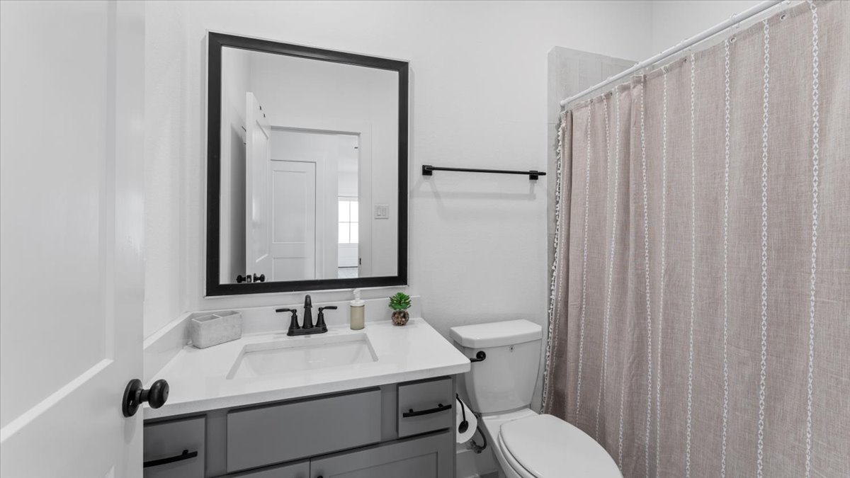 Bright bathroom with vanity, mirror, and shower-tub combo in a furnished home rental in Cypress Texas.