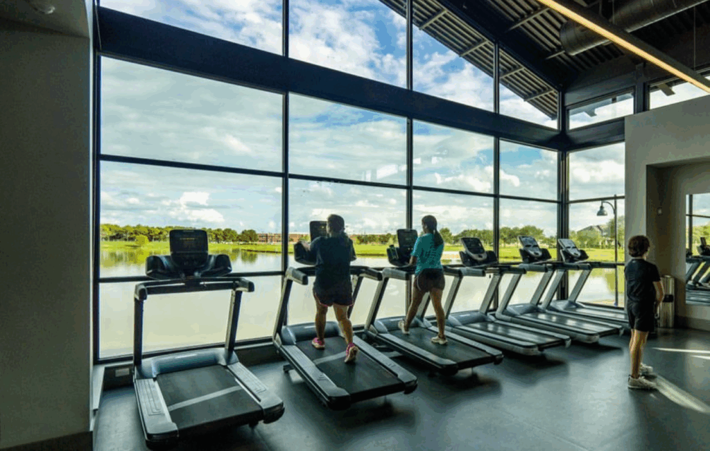 Fitness center with treadmills overlooking a scenic lake, available for guests staying at midterm rentals in Cypress TX.