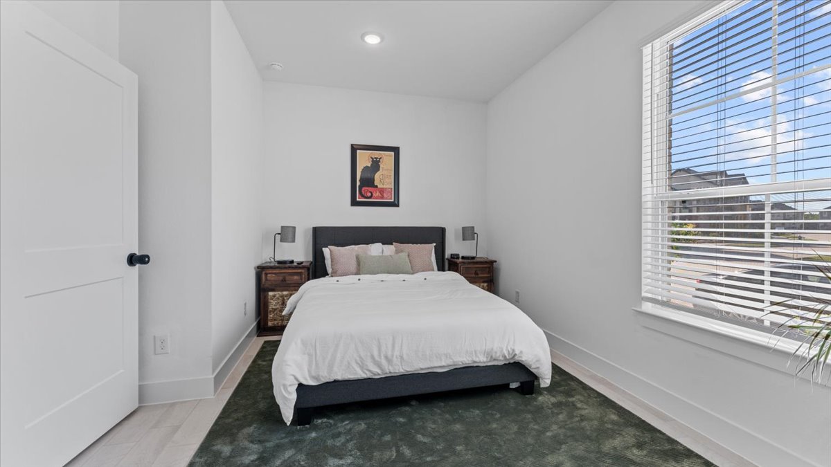 Guest bedroom with queen bed, nightstands, and large window in a furnished home rental in Cypress Texas.